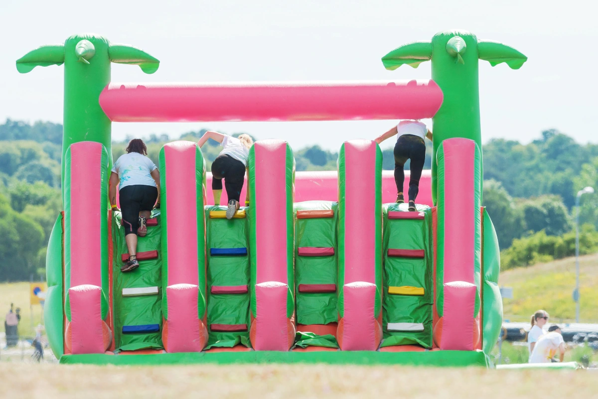 hree girls climbing an obstacle at the color obstacle rush at Gardet in Stockholm. 15 obstacles, 6 colors and 5k running.